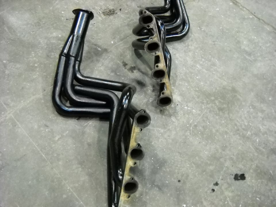 Pair of black long-tube V8 exhaust headers lying flange-up on a concrete floor