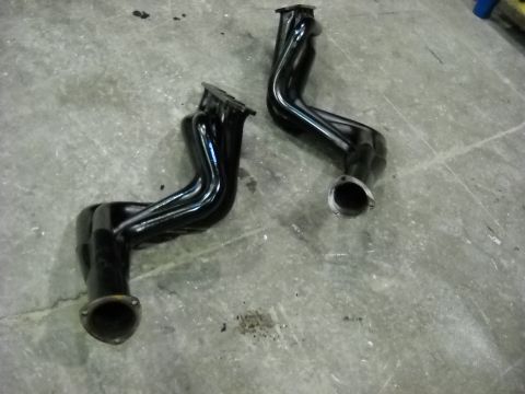 1978 Ford Bronco - A matched pair of black-painted four-into-one V8 tubular exhaust headers laid out on a concrete shop floor, showing the flanged head ports…