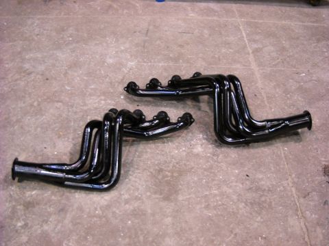 1978 Ford Bronco - A matched pair of glossy black long-tube exhaust headers lying side by side on a bare concrete floor, each with four primary tubes sweeping…
