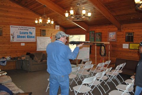 1979 Ford F-150 - A man demonstrates firearm safety indoors at a shooting clinic, with chairs set up for an audience.