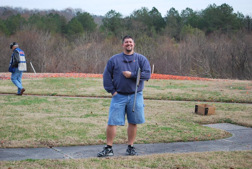 Man with shotgun at skeet range, another person in background
