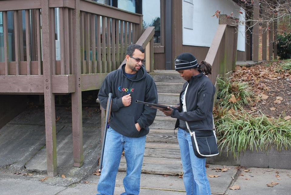 Man in Google hoodie and woman in black jacket examine a shotgun