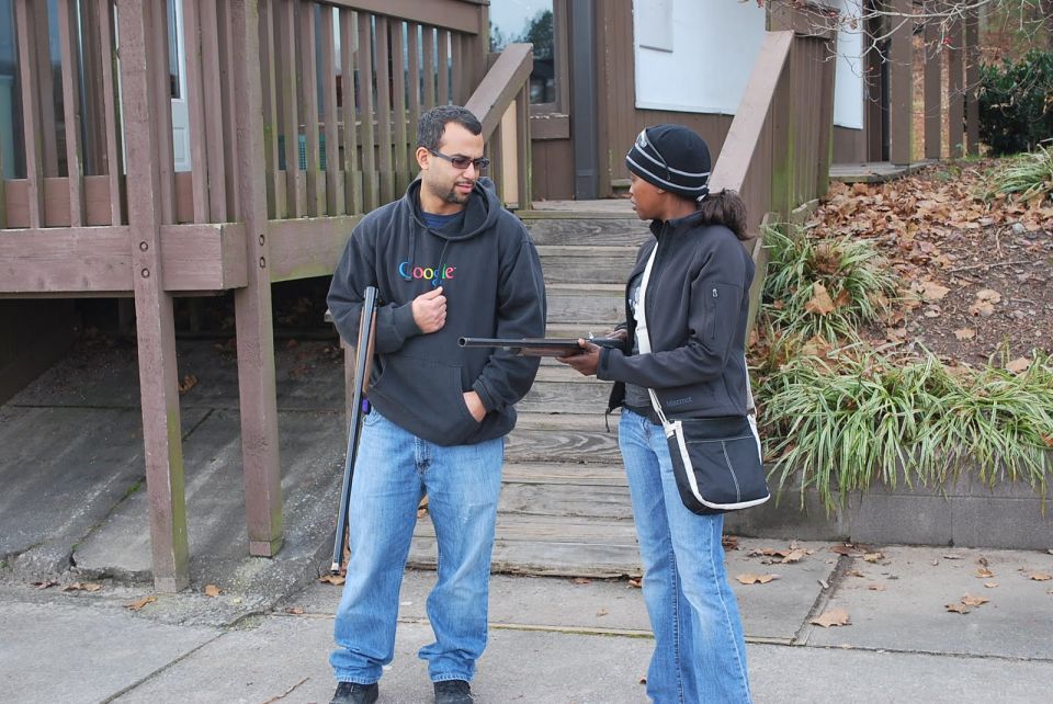 Man in Google hoodie and woman in beanie stand outside with shotguns