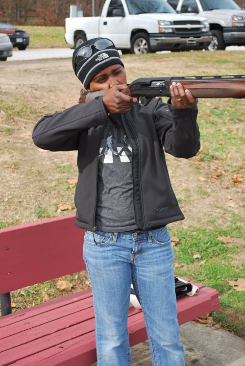 1979 Ford F-150 - A woman takes aim with a shotgun during an outdoor activity, with two pickup trucks visible behind her.
