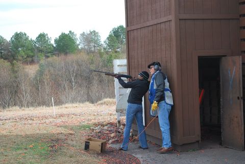 1979 Ford F-150 - Two people practice shooting at a clay pigeon range, with a wooden shelter in the background.