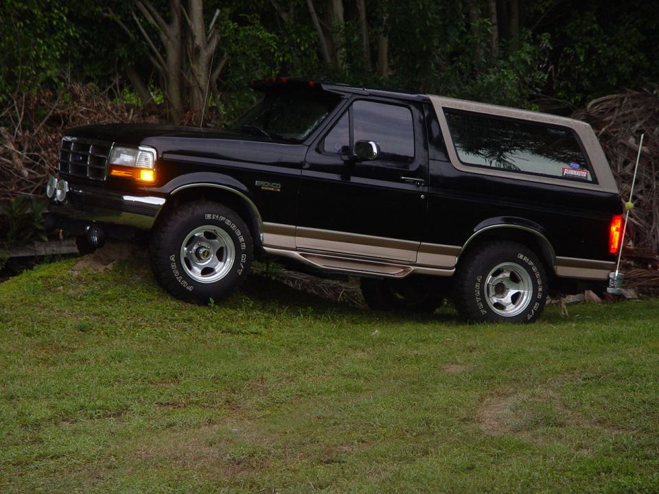 Black 1996 Ford Bronco with tan trim and roof, parked on a grassy incline