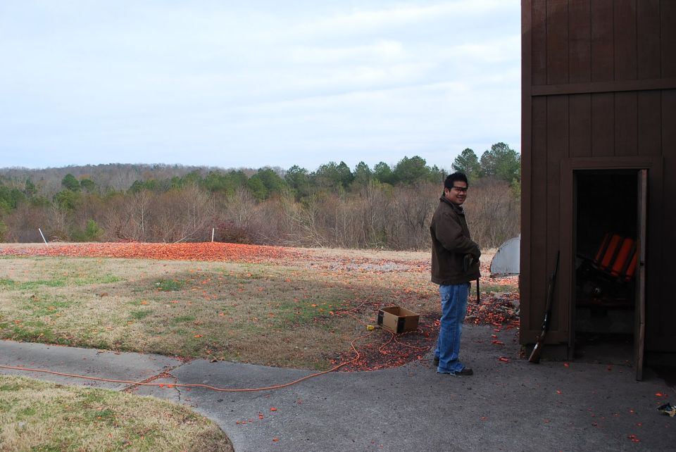 man standing next to a building at a shooting range, with clay targets scattered on the ground