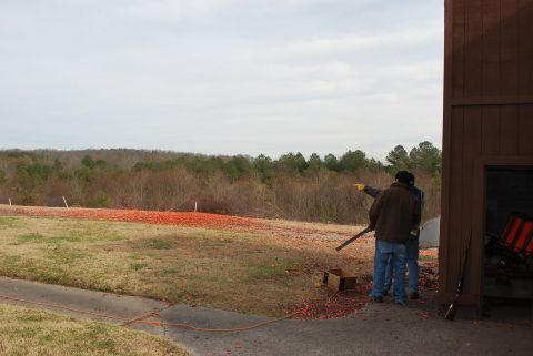 1979 Ford F-150 - A shooting range scene with two individuals observing the field, scattered clay targets, and a wooden building.