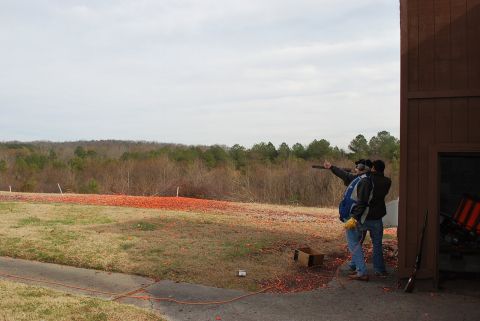 1979 Ford F-150 - Two men participate in a clay pigeon shooting event on a cloudy day, with a wooded area in the background.