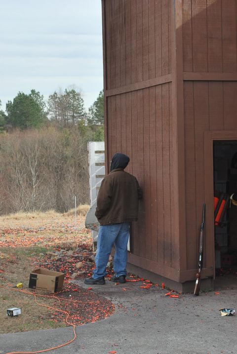 1979 Ford F-150 - A person stands by a wooden structure at what appears to be a shooting range, with a shotgun and scattered clay targets visible.
