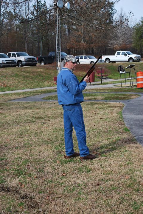 1979 Ford F-150 - A man stands at a shooting range holding a shotgun, with several vehicles parked in the background.