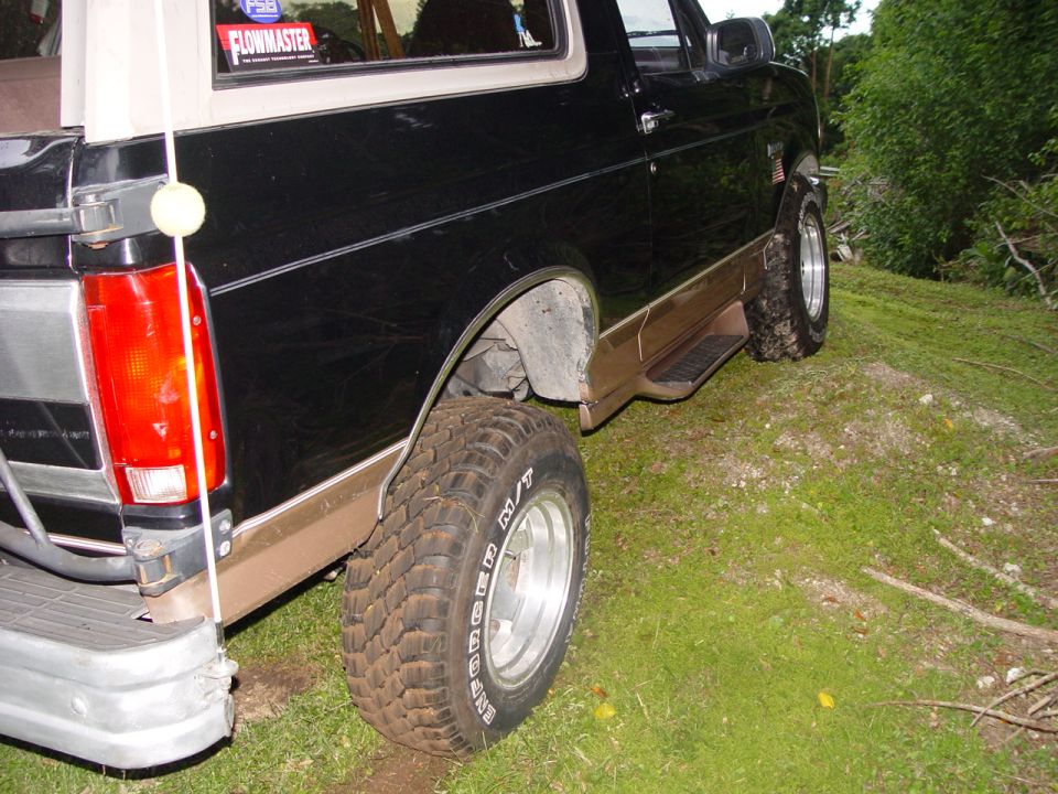 Rear quarter view of a black and tan Ford Bronco parked on a grassy hill