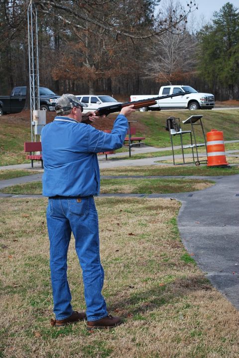 1979 Ford F-150 - A man takes aim with a shotgun at a clay shooting range, with a white pickup truck visible in the background.