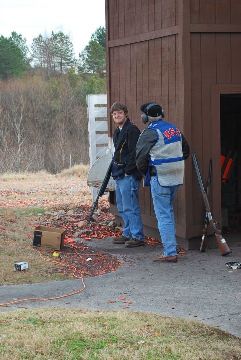 1979 Ford F-150 - Two men with shotguns are at a shooting range, with clay targets scattered on the ground. One man wears a vest with "USA" on it.