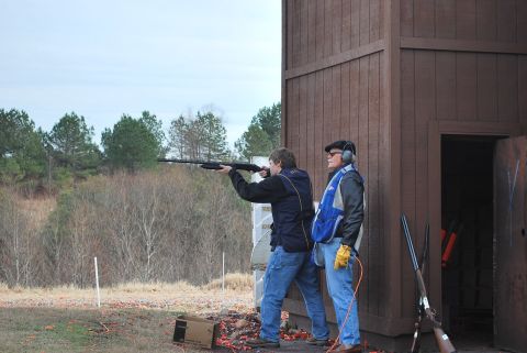 1979 Ford F-150 - Men practice shooting at a range with shotguns, with a wooden structure and trees in the background.