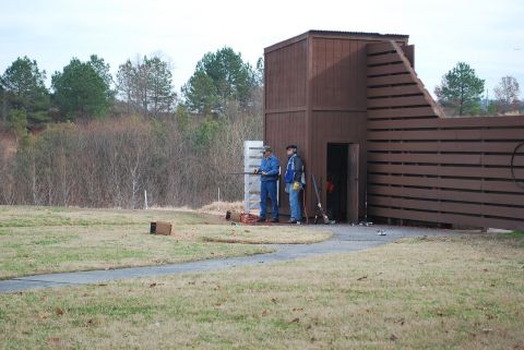 1979 Ford F-150 - A scene at an outdoor shooting range with two individuals near a wooden structure and a slatted fence.