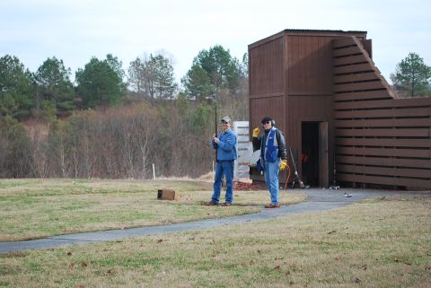 1979 Ford F-150 - Two men are at a shooting range, one holding a shotgun, with a wooden building in the background.