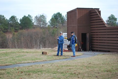 1979 Ford F-150 - Two men are at a shooting range, with a wooden structure in the background. One man is holding a shotgun.