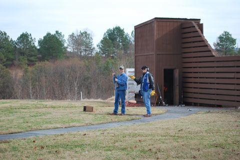1979 Ford F-150 - Two men with shotguns are at a shooting range, with a wooden structure in the background.