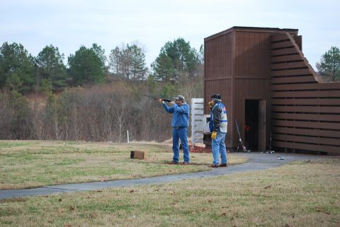 1979 Ford F-150 - A clay shooting event is underway with participants at the ready near a wooden structure.