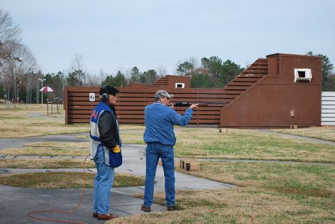1979 Ford F-150 - Two men participate in a shooting event at an outdoor range with wooden backstops and grassy fields.