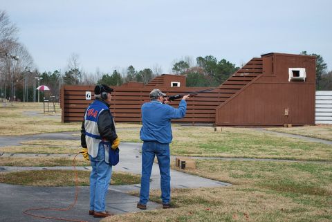 1979 Ford F-150 - Two men participate in a clay pigeon shooting event at an outdoor range, with wooden structures and grassy fields visible.