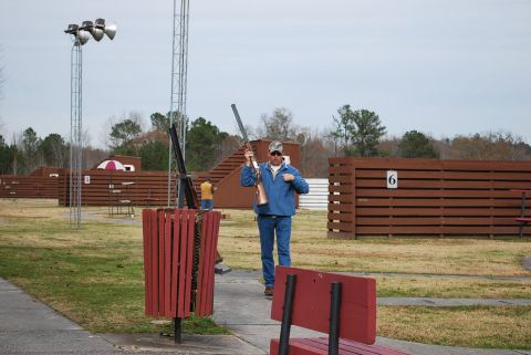1979 Ford F-150 - A man stands with a shotgun at a shooting range, with other participants and facilities in the background.