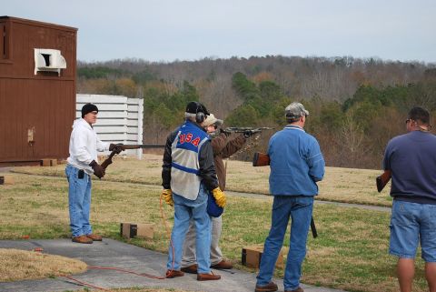 1979 Ford F-150 - People participate in a shooting sport event at an outdoor range with wooded hills in the background.
