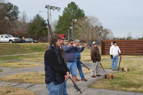 1979 Ford F-150 - People practice shooting at a clay pigeon range with shotguns, while a white pickup truck is parked in the background.