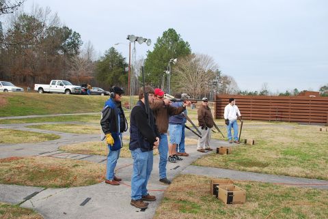 1979 Ford F-150 - Men practice shooting at a clay pigeon range on an overcast day. Vehicles are visible in the background.