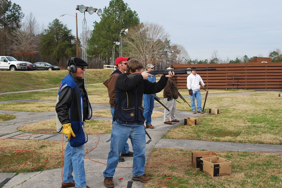 People at a shooting range, one person aiming a shotgun at clay pigeons