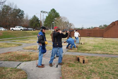 1979 Ford F-150 - Participants practice shooting at a skeet range on an overcast day, with a white pickup truck visible in the distance.