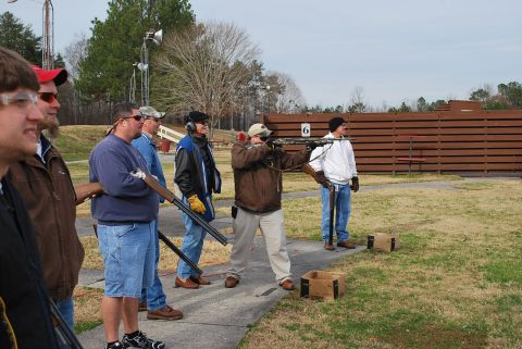 1979 Ford F-150 - Men participate in a shooting event at an outdoor range, with wooden barriers in the background.