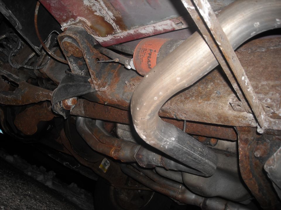 Underside of a vehicle showing rusted exhaust pipes and a fuel filter