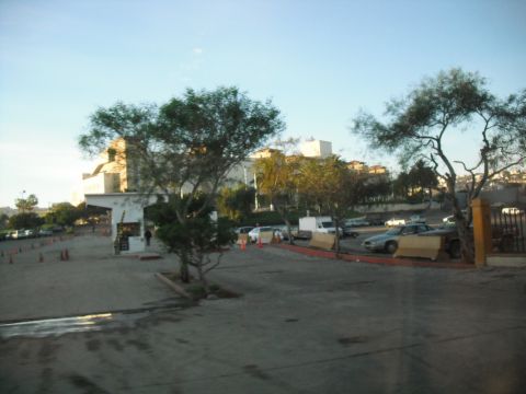 1991 Ford Bronco - A view of a parking lot with several vehicles, trees, and buildings in the background, under a bright sky.