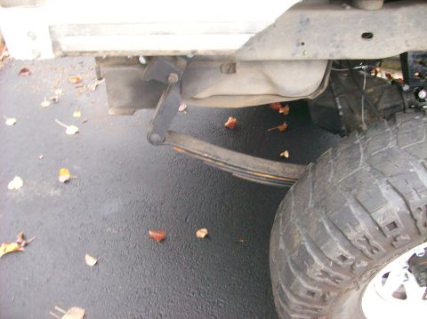 1989 Ford Bronco - A close-up view of the rear suspension and tire of a vehicle, with fallen leaves on the ground.