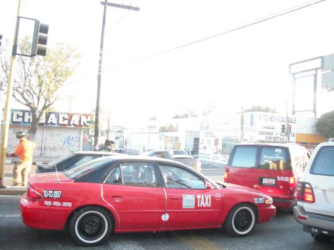 1991 Ford Bronco - A red taxi sedan with white-wall tires is seen in traffic next to other vehicles.