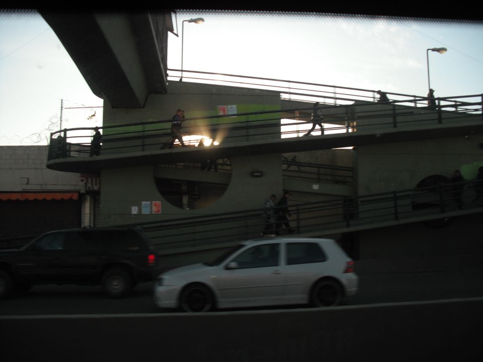 Silver hatchback and black SUV driving on a street with an elevated walkway in the background