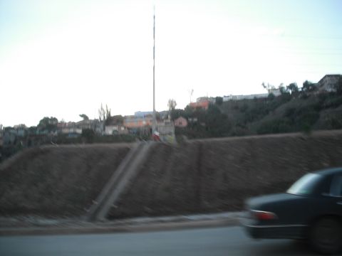 1991 Ford Bronco - A dark sedan is captured in motion, viewed from the rear, with a blurred hillside and buildings in the background.