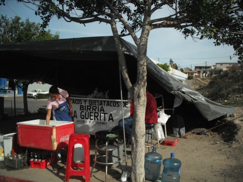 1991 Ford Bronco - A street taco stand is set up under a large black tarp, with a red cooler and water jugs nearby.