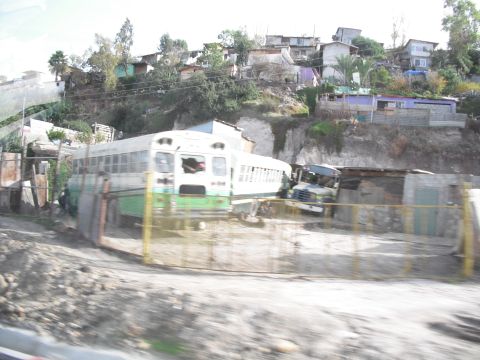 1991 Ford Bronco - Two buses and a truck are parked in a lot with houses built on a steep hillside in the background.