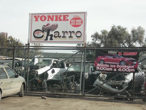1991 Ford Bronco - A junkyard displays wrecked vehicles behind a fence, with signage indicating business hours.