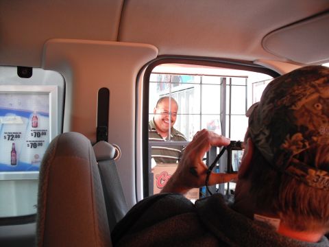1991 Ford Bronco - A person inside a vehicle photographs a smiling employee through a drive-thru window.