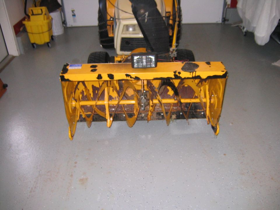 Yellow garden tractor with worn front snowblower attachment on gray epoxy garage floor