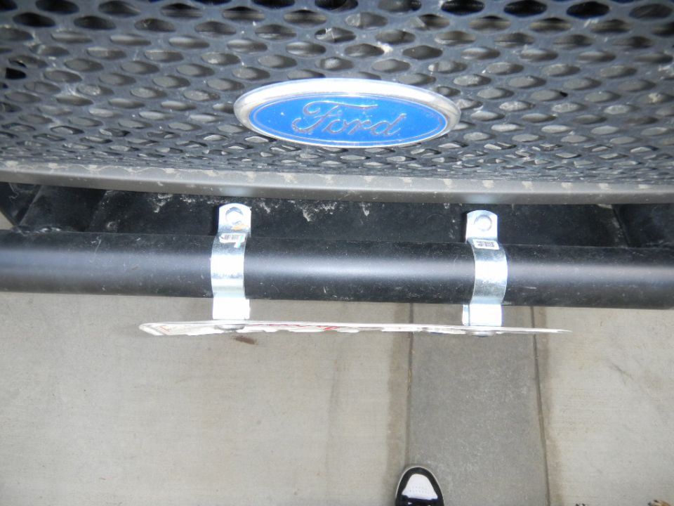 Ford emblem on a black grille above a black bumper bar holding a license plate