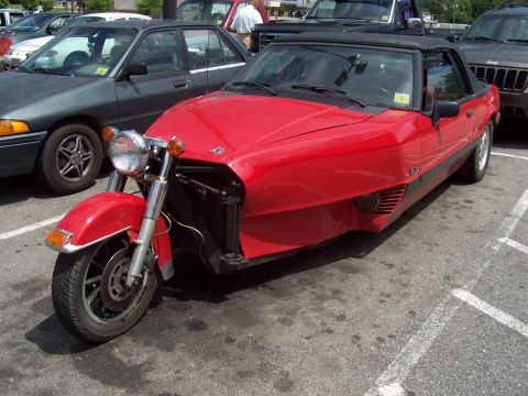 1978 Ford Mustang II - A unique red trike conversion is parked in a lot next to other vehicles.