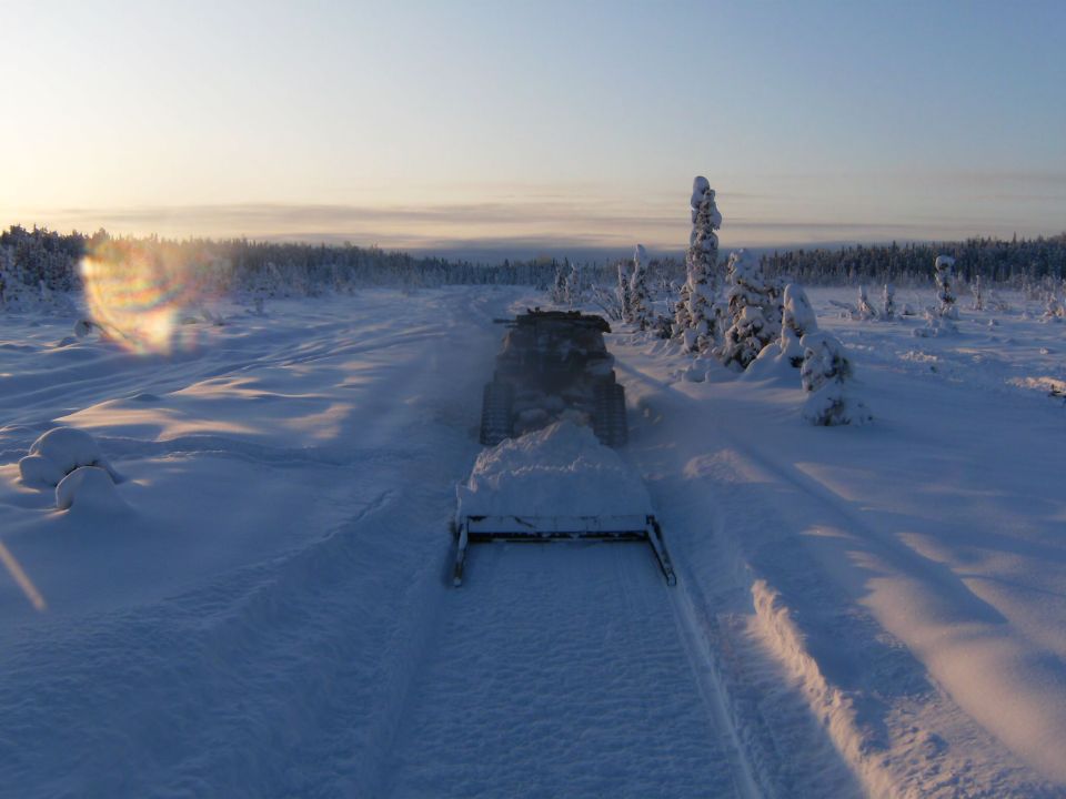 Snowmobile with plow attachment moving forward on a snowy track through a winter landscape