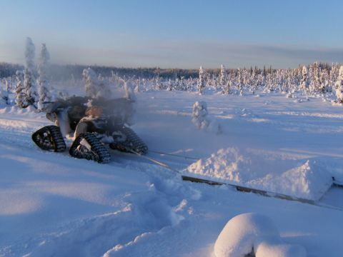 2000 Ford E350 - A tracked vehicle tows a sled of snow through a winter landscape with snow-covered trees in the background.