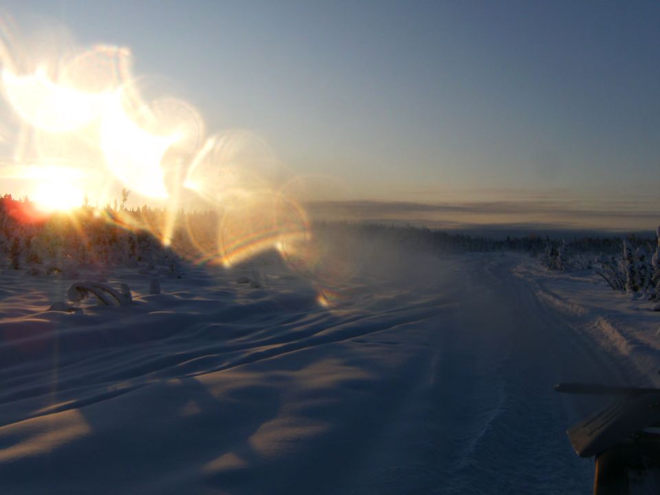 snowy road with sun low on horizon, lens flare