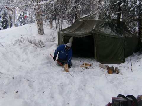 2000 Ford E350 - A person chops wood in the snow near a tent in a winter forest.